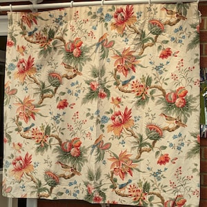 Könnte beinhalten: Cremefarbener Vorhang mit einem botanischen Muster. Es zeigt rote, orange und gelbe Blumen, grüne Blätter und kleine blaue Vögel. Das Design umfasst sich windende braune Äste und kleine blaue Blumengruppen.