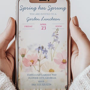 Op de afbeelding: Een smartphone toont een uitnodiging voor een tuinlunch. De tekst "Spring has Sprung" en "Garden Luncheon" zijn zichtbaar. Roze, witte en blauwe bloemen zijn afgebeeld. De datum is 23 april.