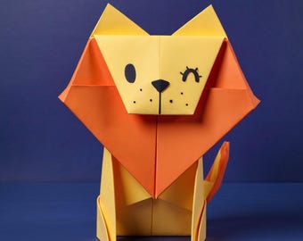 Könnte beinhalten: Eine Origami-Löwenfigur aus gelbem und orangefarbenem Papier. Der Löwe hat ein dreieckiges Gesicht mit einer schwarzen Nase, Schnurrhaaren und zwei verschiedenen Augen: einem schwarzen Kreis und einem schwarzen, zwinkernden Auge.