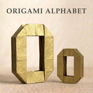 Op de afbeelding: Twee goudkleurige origami letter O vormen, een grote en een kleine, naast elkaar weergegeven. De tekst ORIGAMI ALPHABET staat in donkergrijs bovenaan gedrukt. De letters hebben een gevouwen papierstructuur met scherpe, geometrische randen.