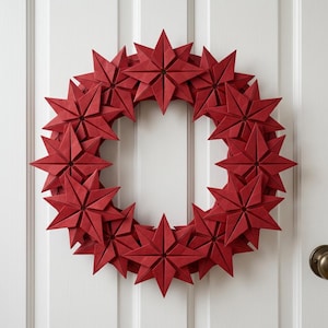 May include: A circular wreath constructed from multiple deep red, eight-pointed origami stars. Each star features sharp, geometric folds and a symmetrical design, arranged in a dense, overlapping pattern to form a continuous ring shape.