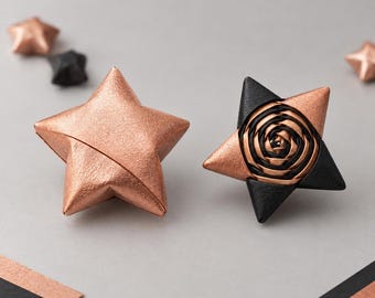 Könnte beinhalten: Zwei fünfzackige Sternornamente. Ein Stern ist aus massivem, metallischem Kupfer mit glatter Oberfläche. Der andere Stern zeigt in der Mitte ein schwarz-kupferfarbenes Spiralrosenmuster mit schwarzen Spitzen und kupferfarbenen Akzenten.