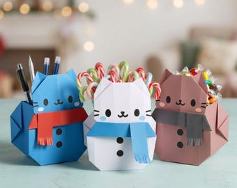 Könnte beinhalten: Drei katzenförmige Papier-Organizer in Blau, Weiß und Braun. Jeder hat ein aufgedrucktes Gesicht, zwei schwarze Knöpfe und einen Papierschal. Der blaue Organizer enthält Stifte, der weiße Zuckerstangen und der braune kleine verpackte Süßigkeiten.