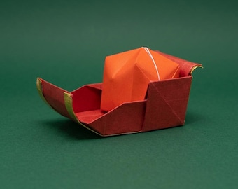 Könnte beinhalten: Ein Origami-Boot aus dunkelrotem Papier mit goldfarbenen Kanten, in dessen Rumpf ein leuchtend orangefarbener, gefalteter Papierblock liegt. Die Struktur weist scharfe geometrische Falten und ein klares, kantiges Design auf.