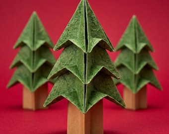 Könnte beinhalten: Drei Origami-Bäume aus strukturiertem grünem Papier mit spitzen, geschichteten Zweigen und Stämmen aus braunem Papier. Die Bäume sind in einer Dreiecksformation angeordnet, wobei ein Baum im Vordergrund steht und zwei weitere leicht unscharf sind.
