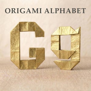 May include: The uppercase and lowercase letter G crafted from gold-colored paper using origami techniques. The paper has a distinct creased texture. Above the letters, the text ORIGAMI ALPHABET is printed in a dark gray, sans-serif font.