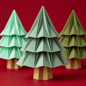 Puede incluir: Tres árboles de papel con follaje plegado y escalonado en tonos verde menta, verde salvia y verde oliva. Cada árbol presenta un diseño geométrico estructurado con pliegues nítidos y angulares y una base hexagonal de color marrón claro.