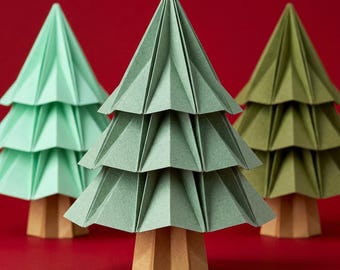 Könnte beinhalten: Drei Papierbäume mit gefaltetem, gestuftem Laub in den Farben Mintgrün, Salbeigrün und Olivgrün. Jeder Baum zeichnet sich durch ein strukturiertes, geometrisches Design mit scharfen, kantigen Falten und einem hellbraunen sechseckigen Sockel aus.