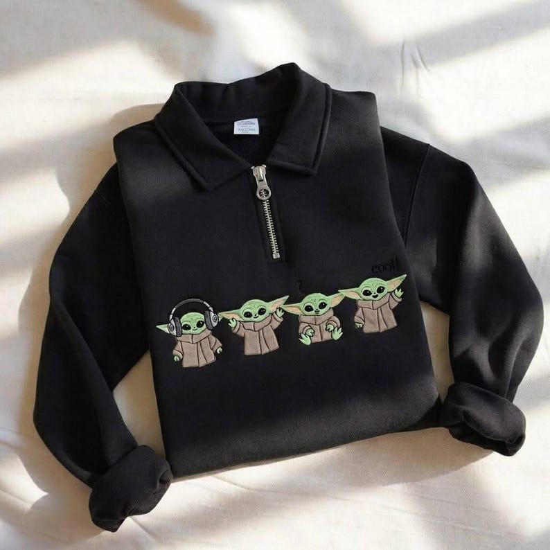 May include: Black sweatshirt with a collared neckline and a silver zipper. The sweatshirt features an embroidered design of four Grogu characters, with the word "cool" above the last character.