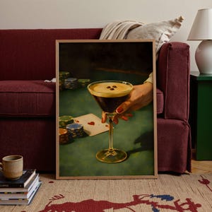 Vertical vintage martini print of an espresso martini and poker poster leaning against a burgundy sofa, creating a stylish coffee cocktail art focal point for eclectic living room decor and gambling wall art lovers.