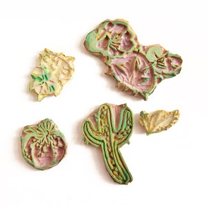 May include: Five wooden stamps with floral and cactus designs. The stamps are painted in shades of green, yellow, and pink.