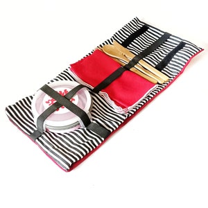 Puede incluir: Un juego de picnic con una esterilla a rayas blancas y negras, servilletas rojas, utensilios de madera y un recipiente redondo. El juego se asegura con bandas elásticas negras. El recipiente tiene un diseño rojo y blanco en la tapa.