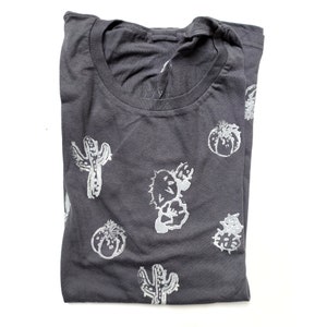 May include: A dark gray t-shirt with a white cactus print. The cactus print is repeated throughout the shirt.