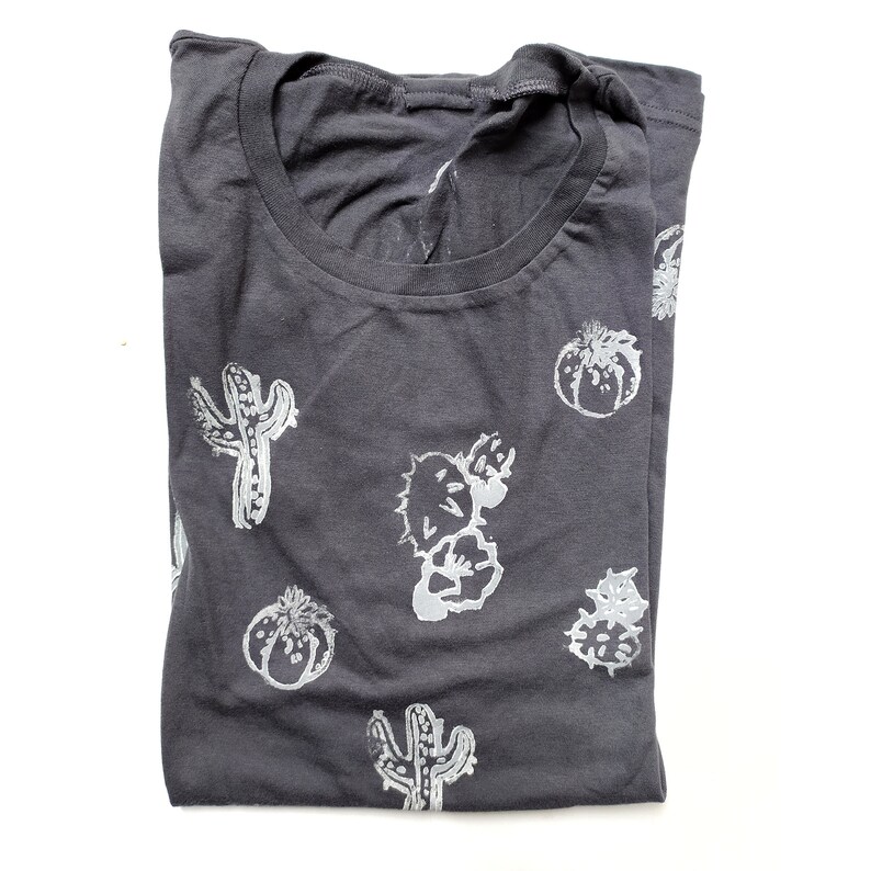 May include: A dark gray t-shirt with a white cactus print. The cactus print is repeated throughout the shirt.