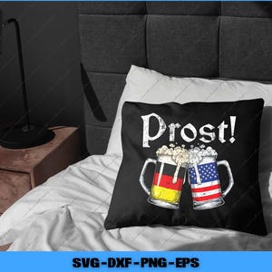 May include: Black throw pillow with the word "Prost!" in white, featuring two beer mugs clinking together. One mug has the German flag design, the other the American flag design. The pillow is on a white bed.