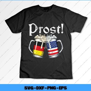 May include: Black t-shirt with the word "Prost!" in white. The design features two beer mugs clinking together, one with the German flag and the other with the American flag. The mugs are filled with beer and foam.