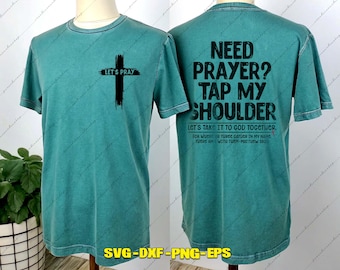 May include: A teal short-sleeve t-shirt featuring a black cross graphic on the front with the text LET'S PRAY. The back displays the black text NEED PRAYER? TAP MY SHOULDER, LET'S TAKE IT TO GOD TOGETHER, and FOR WHERE TWO OR THREE GATHER IN MY NAME.