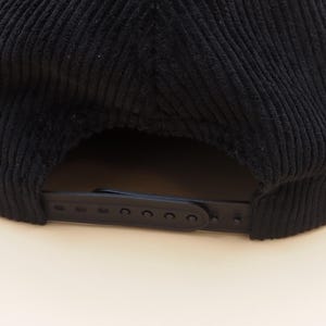 K&ouml;nnte beinhalten: Schwarze Cord-Baseballkappe mit gebogenem Schirm und verstellbarem Riemen. Die Kappe hat ein klassisches sechsteiliges Design und eine strukturierte Krone. Der verstellbare Riemen besteht aus schwarzem Kunststoff.