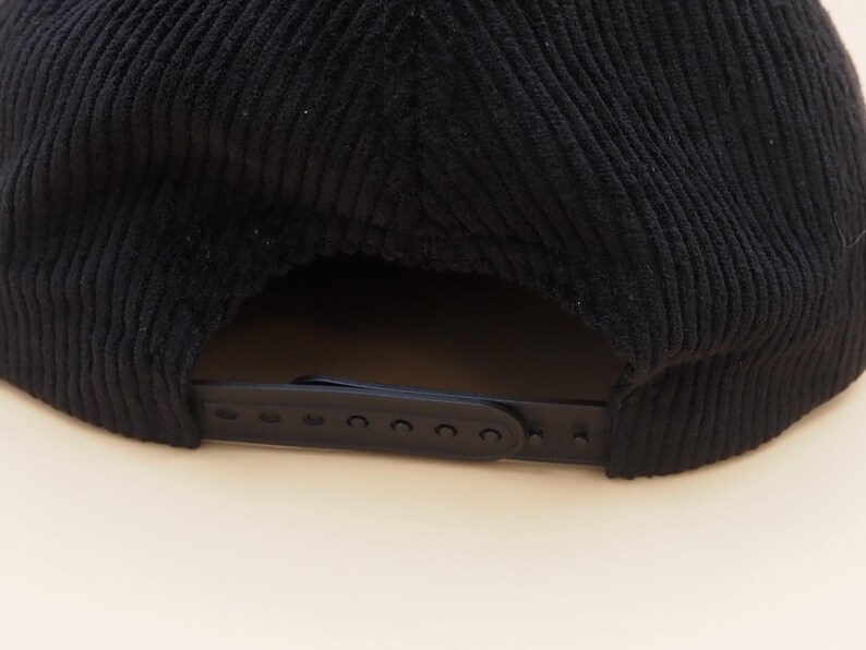 K&ouml;nnte beinhalten: Schwarze Cord-Baseballkappe mit gebogenem Schirm und verstellbarem Riemen. Die Kappe hat ein klassisches sechsteiliges Design und eine strukturierte Krone. Der verstellbare Riemen besteht aus schwarzem Kunststoff.