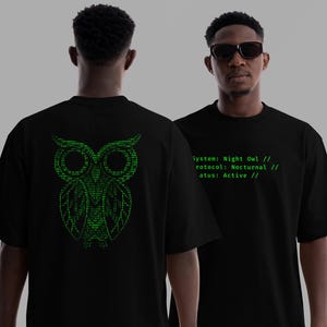 May include: Black t-shirt featuring a green binary code owl design on the back. The front of the shirt displays green text: "System: Night Owl // Protocol: Nocturnal // Status: Active //".