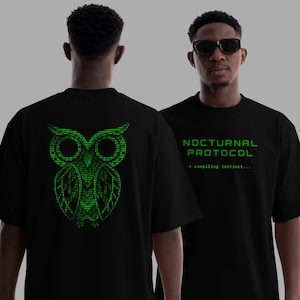 May include: Black t-shirts with green graphics. One shirt displays a binary code owl on the back. The other shirt has the text "NOCTURNAL PROTOCOL" and "compiling instinct..." in green. The shirts are worn by a person.