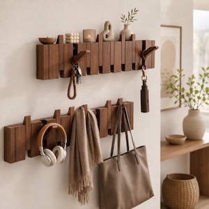 Peut inclure: Deux porte-manteaux muraux horizontaux en bois brun foncé avec un design à lattes verticales. Les supports sont dotés de crochets rétractables, le support supérieur portant des clés et de la décoration, et le support inférieur portant un casque, une écharpe et un sac fourre-tout.