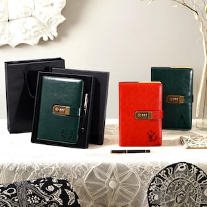 Peut inclure: Journaux en cuir vert et rouge avec serrures à combinaison. Un journal vert est dans une boîte cadeau noire avec un stylo. Le journal rouge a un motif de cerf. Les journaux sont sur une nappe en dentelle blanche.