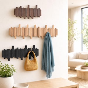 May include: Three wall-mounted coat racks with a vertical slat design, arranged in dark brown, light wood, and black finishes. A mustard yellow woven handbag hangs from the black rack, and a blue fringed scarf hangs from the light wood rack.