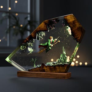 May include: A decorative resin sculpture featuring a wizard on a broomstick, flying over a castle. The sculpture is encased in a clear, geometric shape with a wooden base. The wizard wears a green robe and the castle is green.