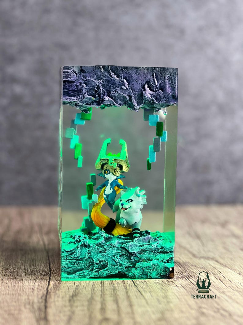 May include: A resin art piece featuring two fantasy characters in a clear rectangular block. The figures are in shades of blue, green, and yellow, set against a textured, glowing green base. The top of the block has a dark, rocky texture.