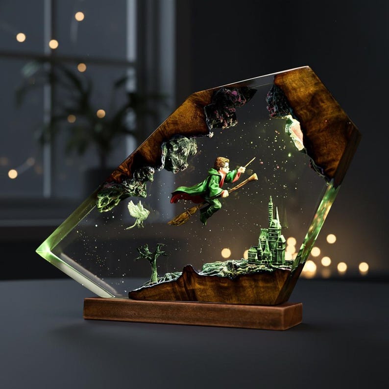 May include: A decorative resin sculpture featuring a wizard on a broomstick, flying over a castle. The sculpture is encased in a clear, geometric shape with a wooden base. The wizard wears a green robe and the castle is green.