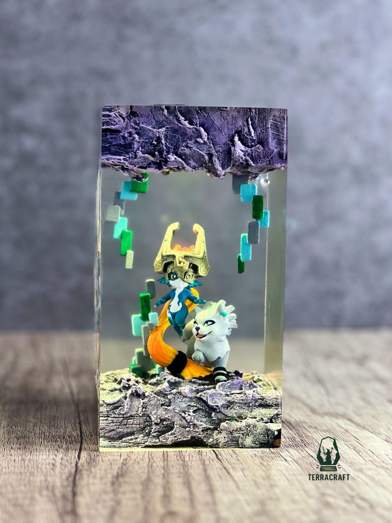 May include: A resin art piece featuring two figurines inside a clear block. One figurine is a blue and white character with a gold crown and orange tail. The other is a white creature with a black and white striped tail. The base is a textured, rocky surface.