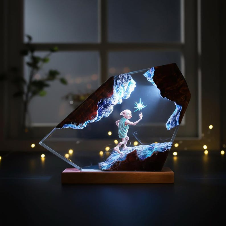 May include: A decorative resin sculpture featuring a character holding a glowing star. The sculpture is set within a geometric frame with a wooden base. The scene is illuminated with blue and white light, creating a magical effect.