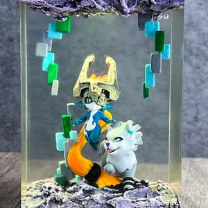 May include: A resin art piece featuring two fantasy characters and a stylized cloud formation. The figures are in shades of blue, white, and gold, with an orange tail. The piece is encased in a clear rectangular block.