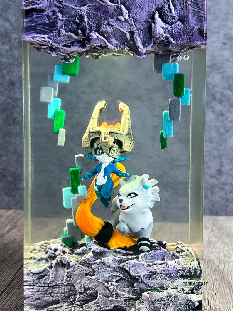 May include: A resin art piece featuring two fantasy characters and a stylized cloud formation. The figures are in shades of blue, white, and gold, with an orange tail. The piece is encased in a clear rectangular block.