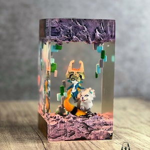May include: A rectangular resin art piece featuring two fantasy characters. One character has a blue and gold outfit with a fox-like tail. The other is a white creature. The piece has a purple, rocky top and a wooden base.
