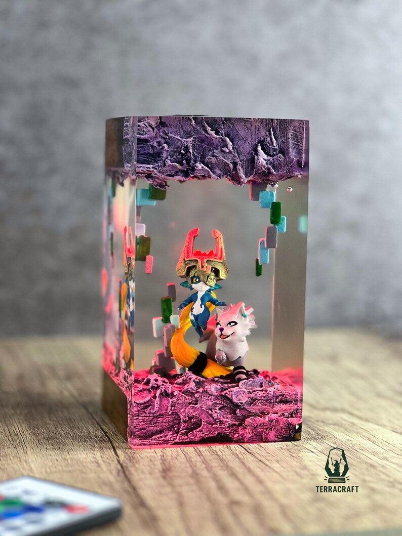 May include: A rectangular resin art piece featuring two fantasy characters inside. The base and top are textured, with a purple and pink color scheme. The characters are a blue and gold figure with a yellow tail and a white and pink creature.