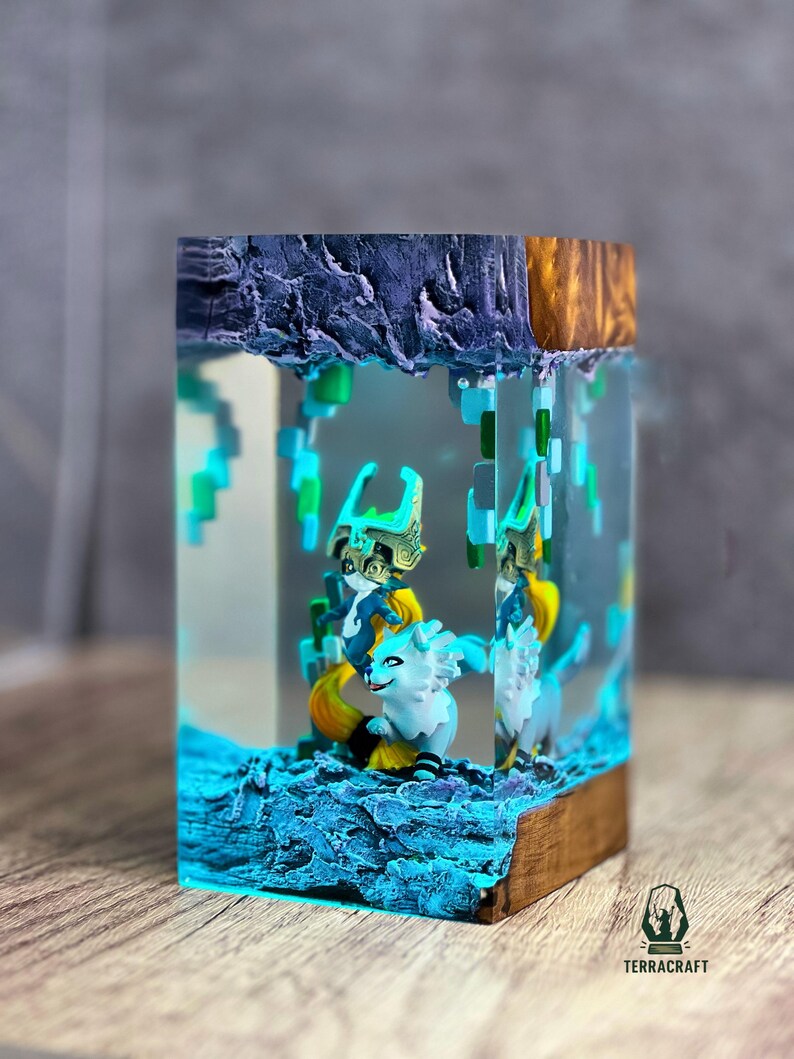 May include: A resin art piece featuring a fantasy scene with two white and yellow creatures, set within a clear block. The scene includes blue and green pixelated elements, and is set on a wooden base. The top of the block has a dark blue and gold textured design. The Terracraft logo is visible.