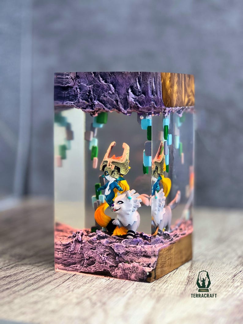 May include: A resin art piece featuring two figures riding white wolves, set within a clear block. The scene includes pixelated elements and a textured, purple base. The top has a gold and purple finish, with the "TERRACRAFT" logo visible.