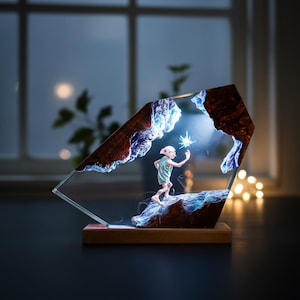 May include: A decorative resin sculpture featuring a character holding a glowing star. The sculpture has a wooden base and a clear, angled frame with brown and blue accents, creating a layered effect. The background is blurred.