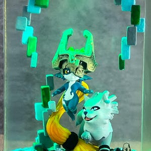 May include: A resin diorama featuring two fantasy figures in shades of blue, green, and yellow. One figure has a large headpiece, and the other is a wolf-like creature. The scene is set within a clear, rectangular block with a textured base.