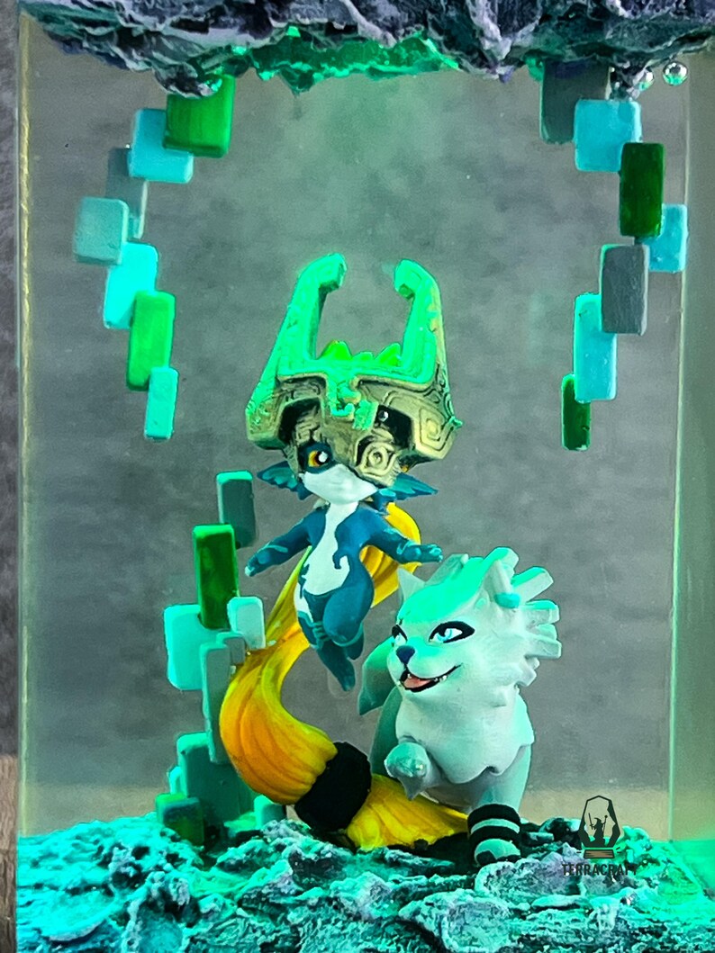 May include: A resin diorama featuring two fantasy figures in shades of blue, green, and yellow. One figure has a large headpiece, and the other is a wolf-like creature. The scene is set within a clear, rectangular block with a textured base.