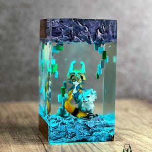May include: A rectangular resin art piece featuring two fantasy creatures in a blue and teal environment. The base is a dark wood. The piece is illuminated with blue and green lights, creating a magical effect. The art piece is labeled with the word "TERRACRAFT".