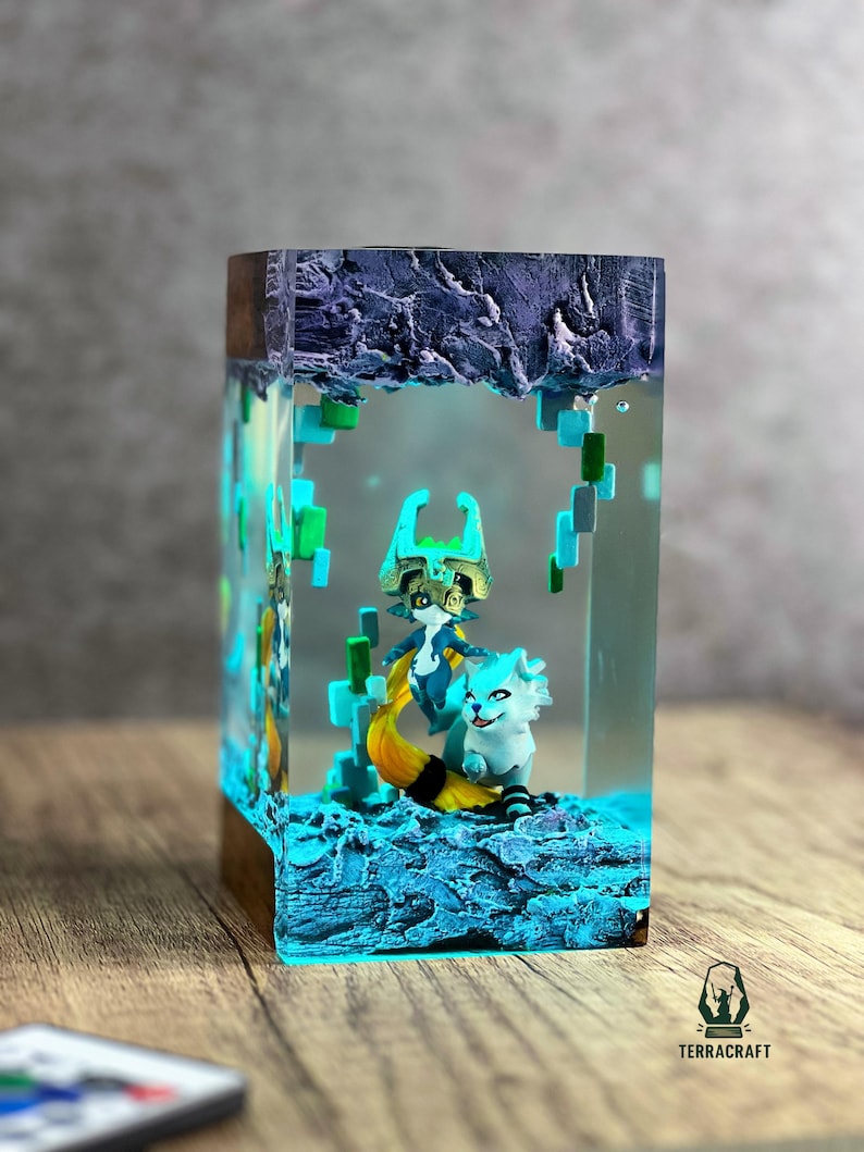 May include: A rectangular resin art piece featuring two fantasy creatures in a blue and teal environment. The base is a dark wood. The piece is illuminated with blue and green lights, creating a magical effect. The art piece is labeled with the word "TERRACRAFT".