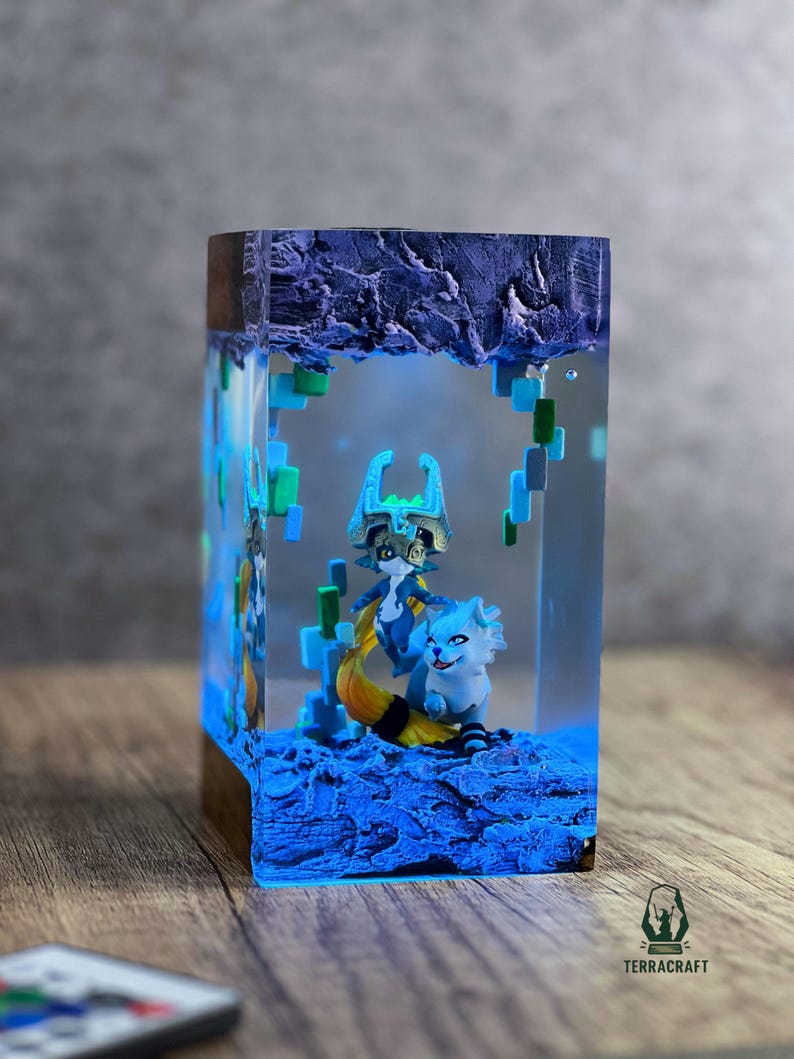 May include: A rectangular resin art piece featuring two fantasy creatures in a blue and green environment. The artwork is encased in clear resin with a wooden base and top. The piece is illuminated with blue light, creating a glowing effect.