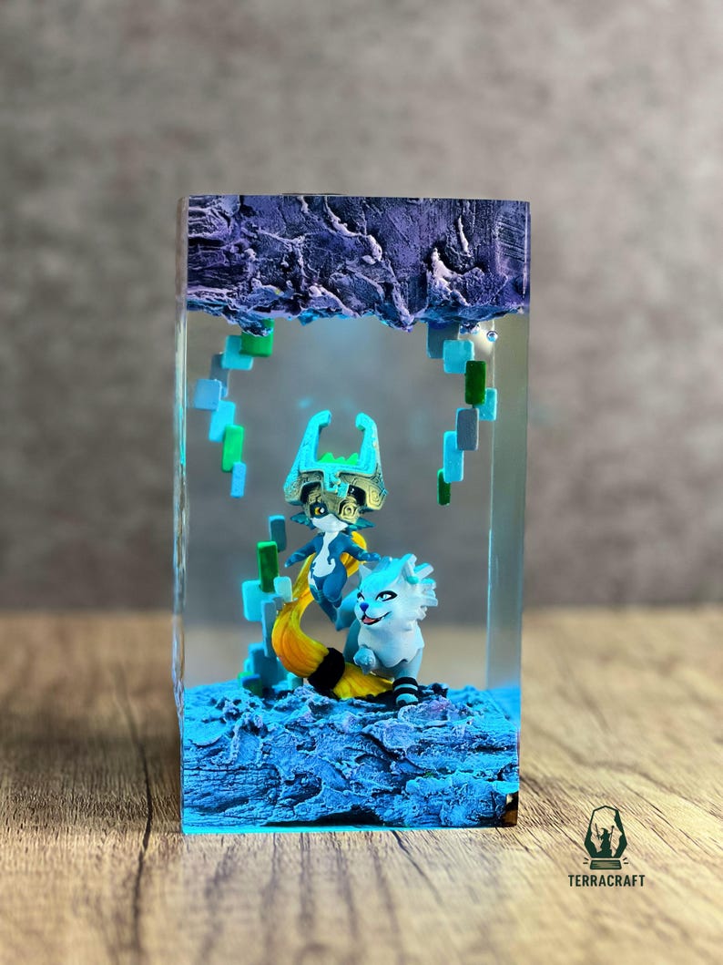 May include: A resin art piece featuring two fantasy characters inside a clear rectangular block. The characters are in shades of blue, white, and gold, set against a textured blue base and a purple, cloud-like top. The piece has a logo in the bottom right corner.
