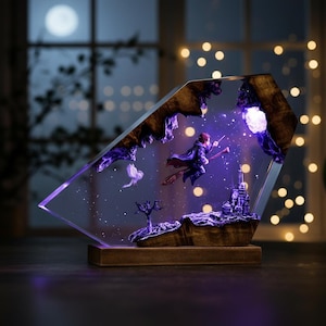 May include: A decorative resin sculpture featuring a wizard on a broomstick, a castle, and a bird, all set against a starry night sky. The sculpture is encased in a clear, angled frame with a wooden base, illuminated by purple and white lights.