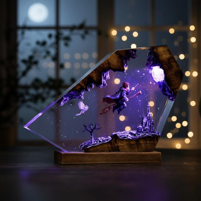 May include: A decorative resin sculpture featuring a wizard on a broomstick, a castle, and a bird, all set against a starry night sky. The sculpture is encased in a clear, angled frame with a wooden base, illuminated by purple and white lights.
