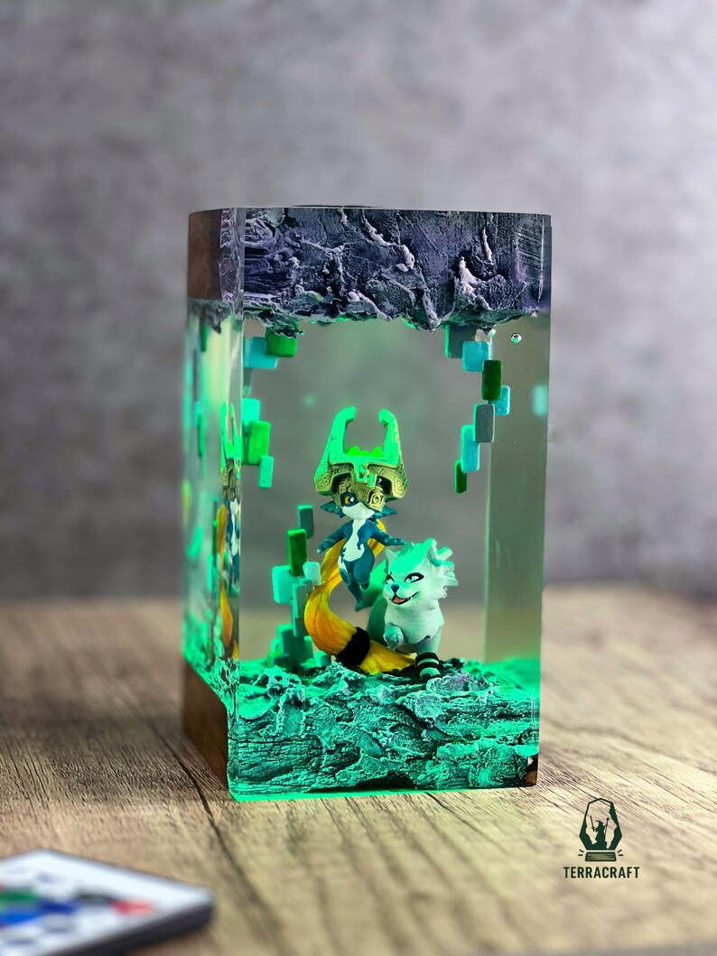 May include: A rectangular resin art piece featuring two fantasy figures inside a glowing green environment. The top and bottom are textured, with a wooden base. The figures are a fox-like creature and a character with a green mask and headdress.