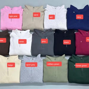 May include: A collection of folded quarter-zip sweatshirts in various colors, including light pink, sand, ash, navy, dark chocolate, white, grey, black, maroon, beige, sport grey, military green, and forest green. Each sweatshirt has a label indicating its color.
